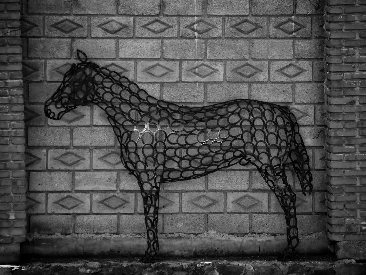 Black and white image of a horse sculpture made from horseshoes on a brick wall in Mexico.